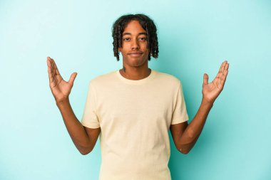 Genç Afrikalı Amerikalı adam mavi arka planda izole edilmiş. Elinde parmakları olan, gülümseyen ve kendinden emin bir şey var..