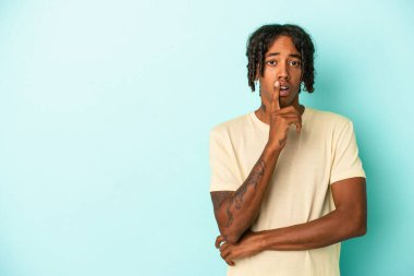 Genç Afrikalı Amerikalı bir adam mavi arka planda izole edilmiş şüpheli ve şüpheci bir ifadeyle yana bakıyor..