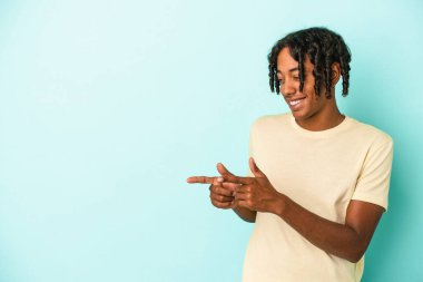 Genç Afrikalı Amerikalı adam mavi arka plan noktalarında izole edilmiş, başparmak uzakta, gülüyor ve kaygısız..