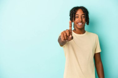 Genç Afrikalı Amerikalı bir adam mavi arka planda izole edilmiş. Bir numarayı parmağıyla gösteriyor..