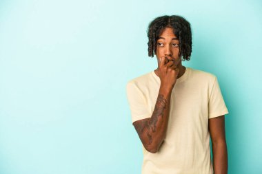 Genç Afrikalı Amerikalı bir adam mavi arka planda izole edilmiş rahat bir şekilde bir şeyin fotokopi odasına baktığını düşünüyor..