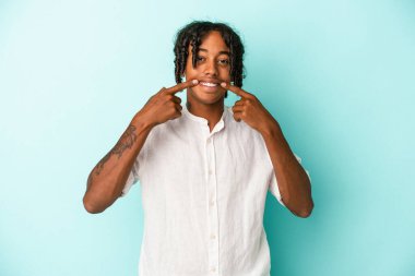 Genç Afrikalı Amerikalı adam mavi arka planda izole edilmiş gülümsüyor, parmaklarını ağıza doğrultuyor..