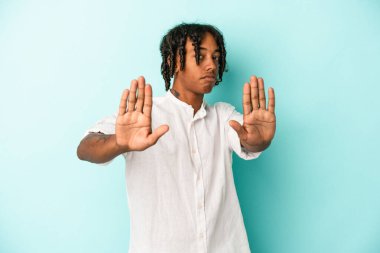 Genç Afrikalı Amerikalı bir adam mavi arka planda izole edilmiş, elini uzatmış, dur işareti göstererek, seni engelliyor..