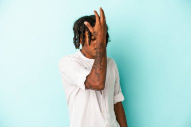 Genç Afrikalı Amerikalı bir adam mavi arka planda izole edilmiş bir şekilde bir şeyi unutuyor. Alnına avuç içi ve kapalı gözlerle vuruyor..