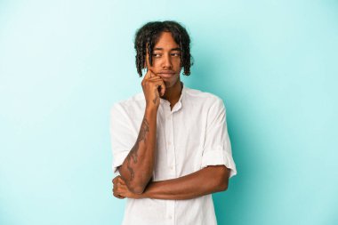Genç Afrikalı Amerikalı bir adam mavi arka planda izole edilmiş, kafası karışmış, şüpheli ve güvensiz hissediyor..