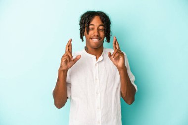Genç Afro-Amerikalı adam mavi arka planda izole edilmiş şans diliyor.