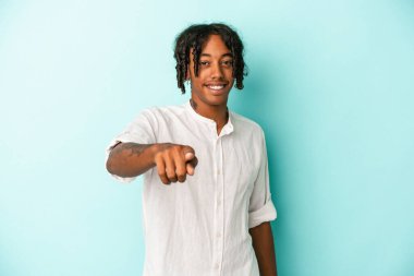 Genç Afro-Amerikalı adam mavi arka planda izole edildi. Neşeli gülümsemeler ön tarafı işaret ediyor..