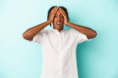 Genç Afrikalı Amerikalı bir adam mavi arka planda izole edilmiş. Şaşırmış ve şok olmuş..
