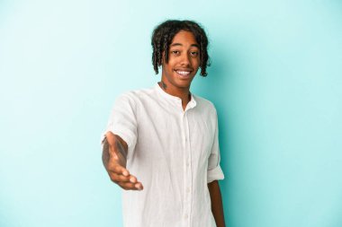 Genç Afro-Amerikan adam mavi arka planda izole edildi. Kameraya doğru elini uzatarak selamlama hareketi yapıyor..