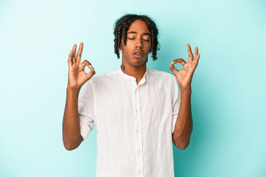 Genç Afrikalı Amerikalı erkek mavi arka planda izole edilmiş yoğun bir günün ardından rahatlıyor, yoga yapıyor..