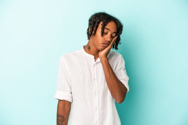 Mavi arka planda izole edilmiş, sıkılmış, yorgun ve dinlenmeye ihtiyacı olan genç Afrikalı Amerikalı bir adam..