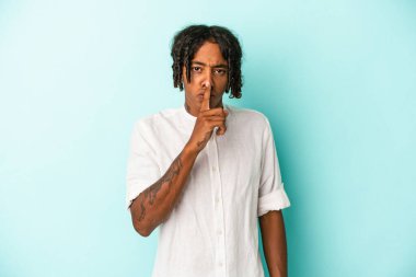 Genç Afrikalı Amerikalı bir adam mavi arka planda izole edilmiş bir şekilde sır saklıyor ya da sessizlik istiyor..