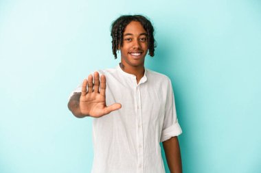 Genç Afro-Amerikalı adam mavi arka planda izole edilmiş. Gülümsüyor. Beş numarayı parmaklarıyla gösteriyor..