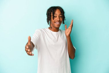 Mavi arka planda izole edilmiş genç Afrikalı Amerikalı adam kameraya sarıldığı için kendinden emin hissediyor..