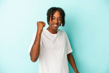 Genç Afrikalı Amerikalı bir adam mavi arka planda izole edilmiş tasasız ve heyecanlı bir şekilde tezahürat yapıyor. Zafer konsepti.