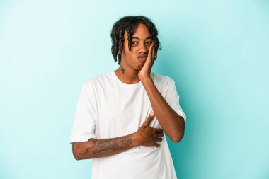 Mavi arka planda izole edilmiş genç Afrikalı Amerikalı adamın yanakları şişer, yorgun bir ifadesi vardır. Yüz ifadesi kavramı.