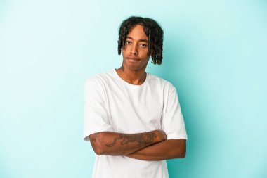 Genç Afro-Amerikalı adam mavi arka planda izole edilmiş. Mutsuz. Kameraya alaycı bir ifadeyle bakıyor..