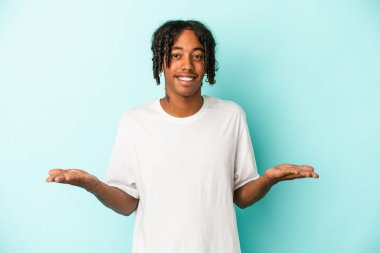 Mavi arka planda izole edilmiş genç Afrikalı Amerikalı adam kollarıyla ölçek oluşturuyor, mutlu ve kendinden emin hissediyor..