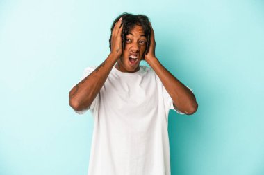 Genç Afro-Amerikalı adam mavi arka planda izole edilmiş kulakları kulaklarıyla kapatıyor çok fazla ses duymamaya çalışıyor..