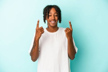 Mavi arka planda izole edilmiş genç Afrikalı Amerikalı iki parmağı da boş bir alan gösteriyor..