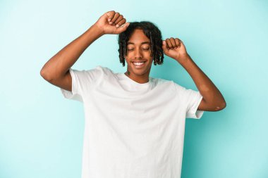 Genç Afrikalı Amerikalı adam mavi arka planda izole edilmiş özel bir günü kutluyor, atlıyor ve enerjiyle kollarını kaldırıyor..