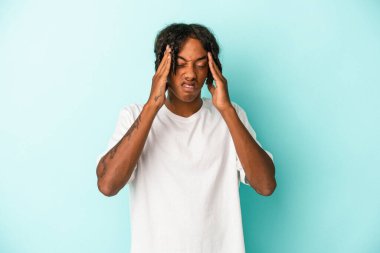 Genç Afrikalı Amerikalı bir adam mavi arka planda izole edilmiş, başı ağrıyor, yüzüne dokunuyor..