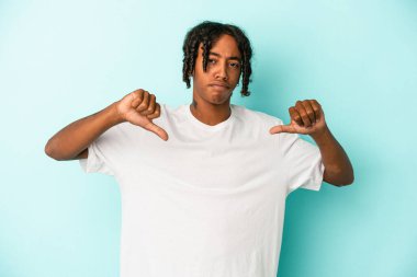 Genç Afro-Amerikalı adam mavi arka planda izole edilmiş, baş parmağını aşağı gösteren, hayal kırıklığı konsepti.