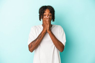 Genç Afro-Amerikalı adam mavi arka planda izole edilmiş ağzı kapalı ve elleri endişeli görünüyor..