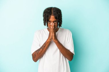 Genç Afrikalı Amerikalı adam mavi arka planda izole edilmiş dua ediyor, bağlılık gösteriyor, dindar biri ilahi ilham arıyor..