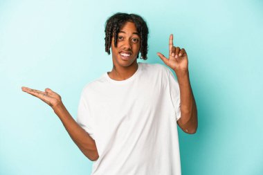 Genç Afrikalı Amerikalı bir adam mavi arka planda izole edilmiş ve elinde bir ürün tutuyor..