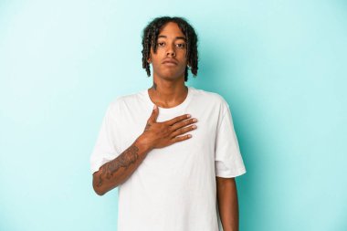 Genç Afrikalı Amerikalı adam mavi arka planda izole edilmiş bir şekilde yemin ediyor, elini göğsüne koyuyor..