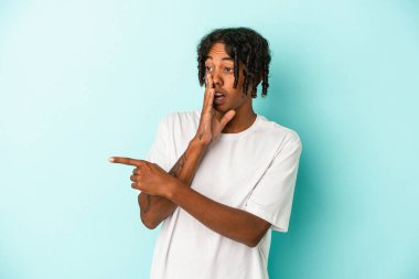 Genç Afrikalı Amerikalı bir adam mavi arka planda izole edilmiş. Dedikodu yapıyor, bir şeyleri bildiriyor..