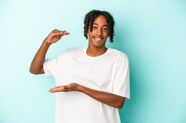 Genç Afrikalı Amerikalı adam mavi arka planda izole edilmiş. Elinde parmakları olan, gülümseyen ve kendinden emin bir şey var..