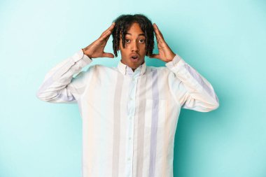 Genç Afro-Amerikan erkeği mavi arka planda izole edilmiş bir şekilde zaferi ya da başarıyı kutluyor. Şaşırmış ve şok olmuş..