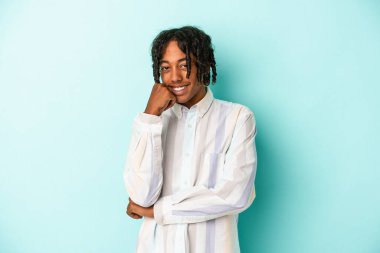 Genç Afrikalı Amerikalı adam mavi arka planda izole edilmiş mutlu ve kendinden emin gülümsüyor, elleriyle çenesine dokunuyor..