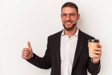 Beyaz arka planda izole edilmiş kahveyi alıp götüren genç beyaz bir adam gülümsüyor ve başparmağını kaldırıyor.