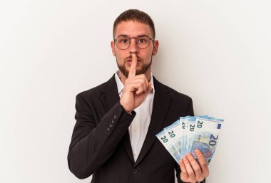 Beyaz arka planda izole edilmiş banknotlar tutan genç beyaz adam bir sır saklıyor ya da sessizlik istiyor..