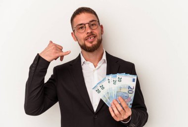 Beyaz arka planda izole edilmiş banknotlar tutan genç bir beyaz iş adamı parmaklarıyla bir cep telefonu hareketi gösteriyor..