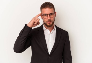 Beyaz arka planda izole edilmiş genç bir beyaz iş adamı şakağı işaret ediyor, düşünüyor, bir göreve odaklanıyor..