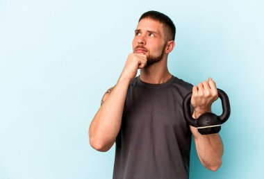 Ketlebell 'i tutan beyaz bir genç mavi arka planda izole edilmiş bir şekilde bir avuç içinde fotokopi alanı ve belinde başka bir el tutuyor..