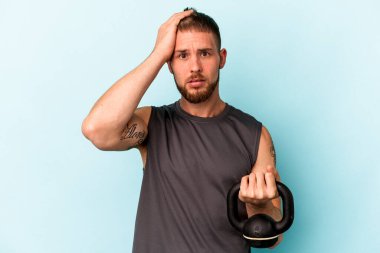 Ketlebell 'i tutan beyaz bir genç, mavi arka planda izole edilmiş, şoka uğramış, önemli bir toplantıyı hatırlıyor..