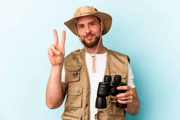 Young caucasian man looking at animals through binoculars isolated on blue background showing number two with fingers.