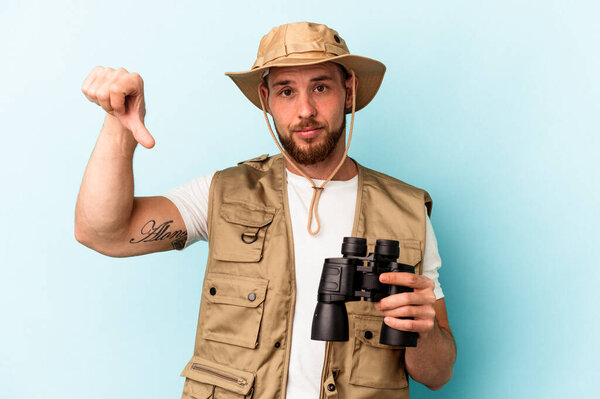 Young caucasian man looking at animals through binoculars isolated on blue background showing a dislike gesture, thumbs down. Disagreement concept.