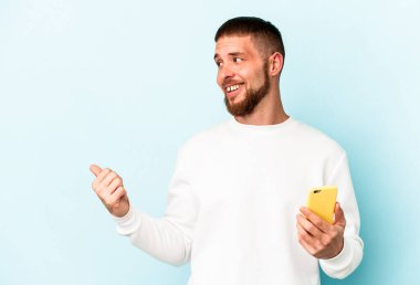 Elinde cep telefonu tutan beyaz bir adam mavi arka plan noktalarında izole edilmiş, başparmak uzakta, gülen ve kaygısız..