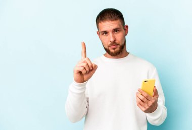 Elinde cep telefonu olan beyaz bir adam mavi arka planda bir numarayı parmağıyla gösteriyor..