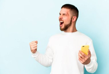 Mavi arka planda cep telefonu tutan genç beyaz adam zaferden sonra yumruğunu kaldırıyor, kazanan konsept.