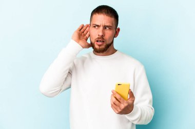 Mavi arka planda cep telefonu tutan beyaz bir adam bir dedikoduyu dinlemeye çalışıyor..