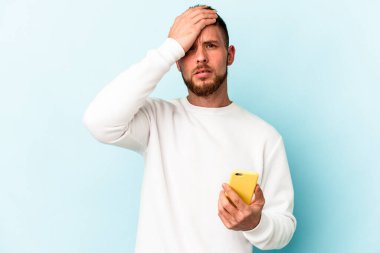 Mavi arka planda cep telefonu tutan genç beyaz adam şok oldu, önemli bir toplantı hatırladı..