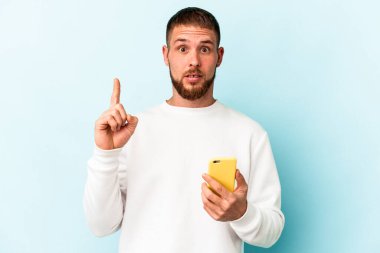 Elinde cep telefonu tutan beyaz bir adam mavi arka planda izole edilmiş. Harika bir fikri var. Yaratıcılık kavramı..