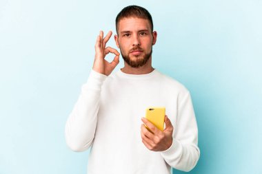 Cep telefonunu elinde tutan beyaz bir adam mavi arka planda izole edilmiş ve parmakları dudaklarında bir sır saklıyor..